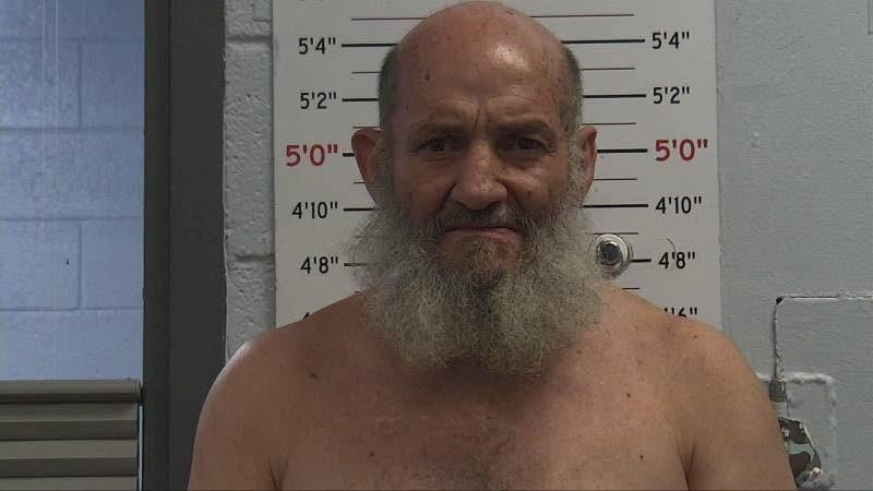 PD booking photo of 5'5" shirtless person facing forward with dark eyes, bald head and long grey facial hair.
