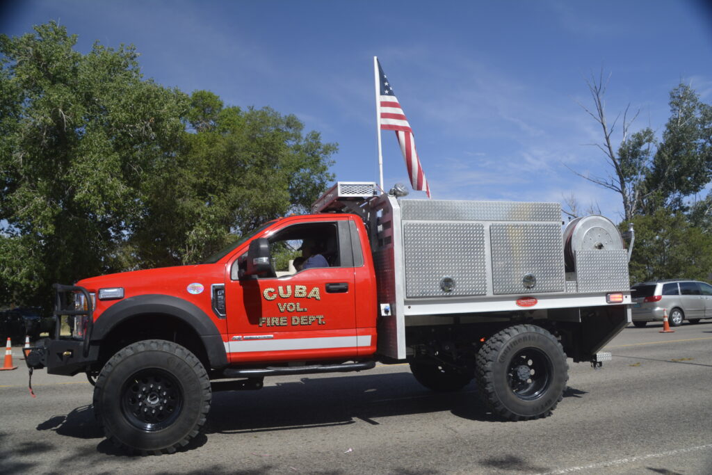 Red CUBA VOL. FIRE DEPT. wildland brush truck in parade with American flag on pole.